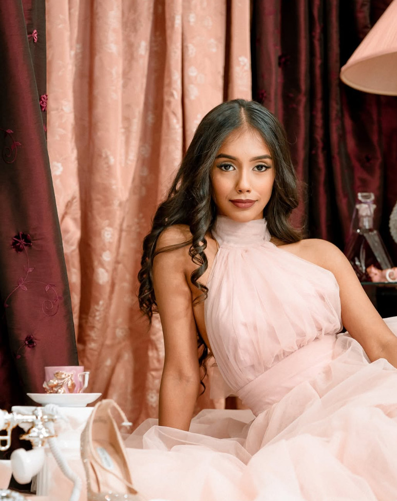 Young woman in soft pink dress seated in an editorial scene